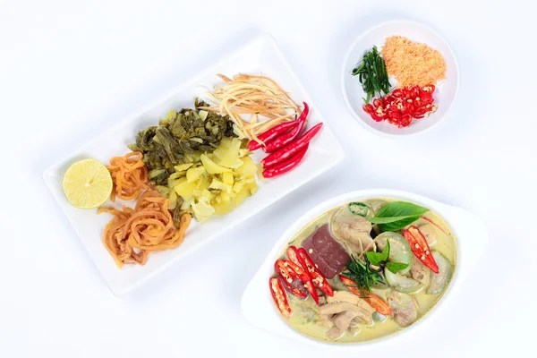 Green chicken curry in coconut milk served with side dish as red pepper,pickle lettuce,minced dried shrimp,sliced correspondents,sliced red chili - kaffir lime leaves,radish and green lemon on white.