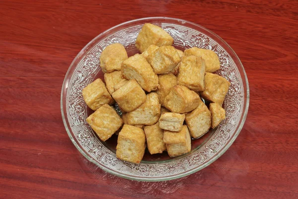 Deep fried of cube soft tofu in glass dish on wood. Top view.