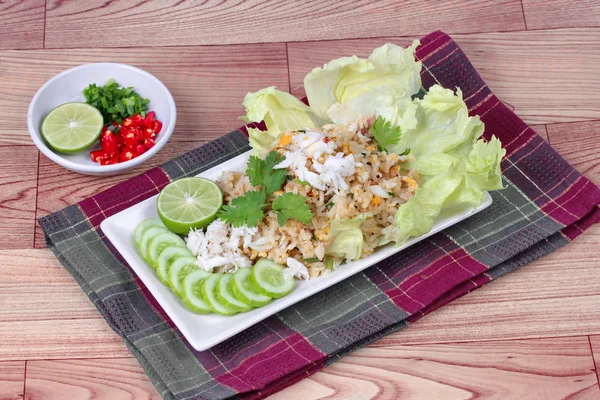 Fried rice with crab topped streamed crab,halve green lemon,sliced cucumber,lettuce and coriander served  spicy  sour filling side dish on wood. Side view.