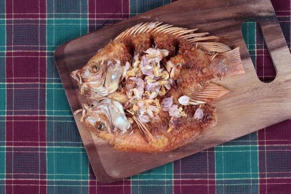 Deep fried fish ,Nile tiapia, with crispy garlic on butcher served. Side view.