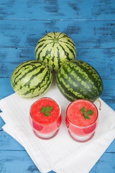 Fresh watermelon juice and three mini watermelons on a blue wooden background
