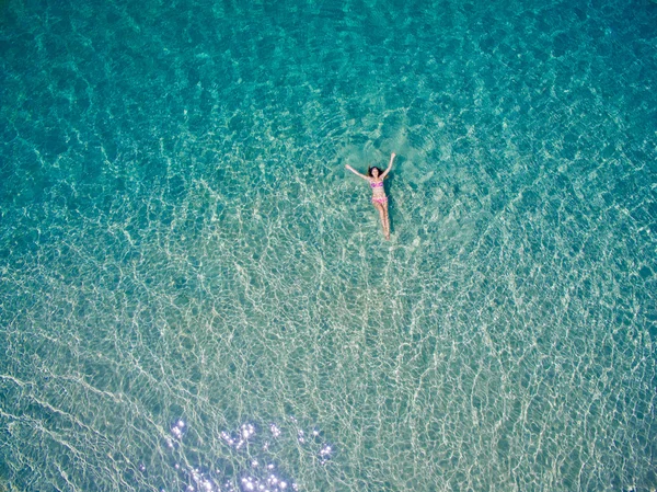 Young woman swimming in the blue water of Andaman sea. Top view. White beach, Phuket, Thailand.