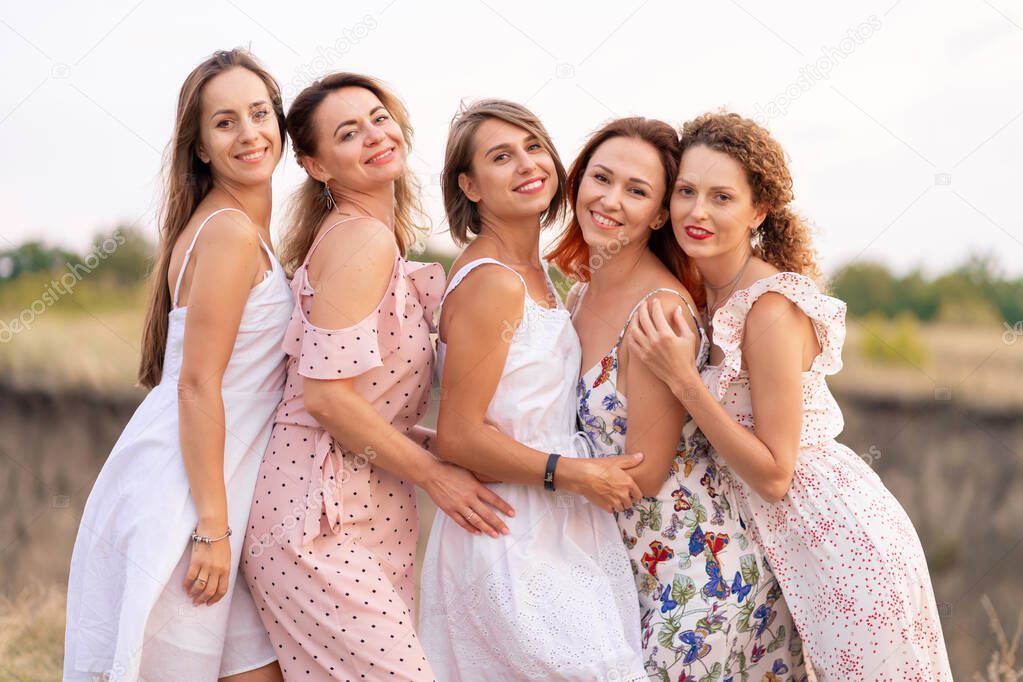 A cheerful company of beautiful girls friends enjoy the company and have fun together in a picturesque place of green hills