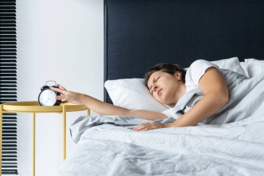 Kız uyumaya devam etmek için sinir bozucu çalar saati kapatıyor. Biraz daha uyu. Zor bir sabah. Kalkma zamanı.