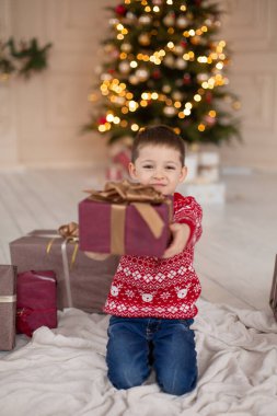Noel ağacının yanında Noel hediyesi kutusuyla kırmızı örülü süveter giyen mutlu küçük çocuğun portresi. Mutlu bir çocukluk. Bir Noel masalı bekliyorum.