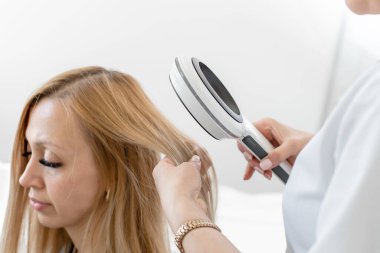 Bir tricholog, hastaların başlarındaki kılların durumunu dermatoskopla inceliyor. Parlak bir kozmetoloji odasında. Dnipro / Ukrayna - 10.27.2019