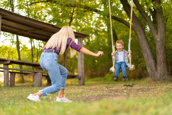 Young Blonde Mom Shakes Her Little Son Swing Green Park — Stock Photo, Image