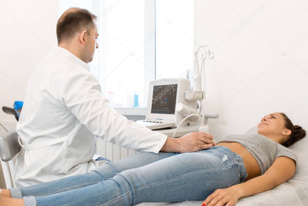 Ultrasound diagnosis of the pelvic organs of the girl. A girl lies on a couch in a white room of ultrasound diagnostics during a diagnostic.