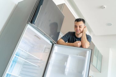 Adam boş buzdolabının yanında yemek yemeden üzgün. Yemek servisi reklamı..