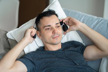 Adam kulaklıkla kanepede yatarken müzikten zevk alıyor. Müzikle rahatlama.