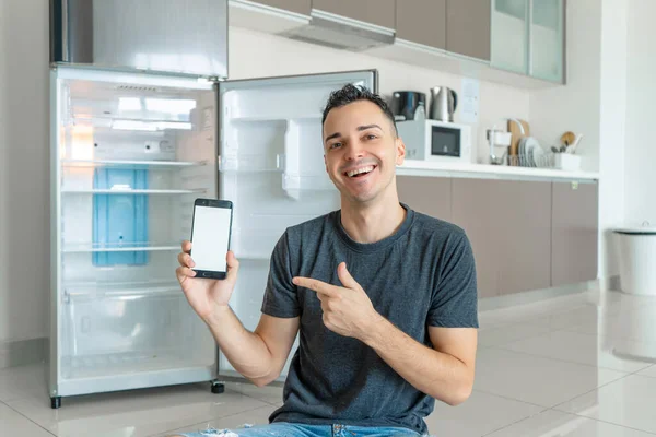 A young guy orders food using a smartphone. Empty refrigerator with no food. Food delivery service advertisement.