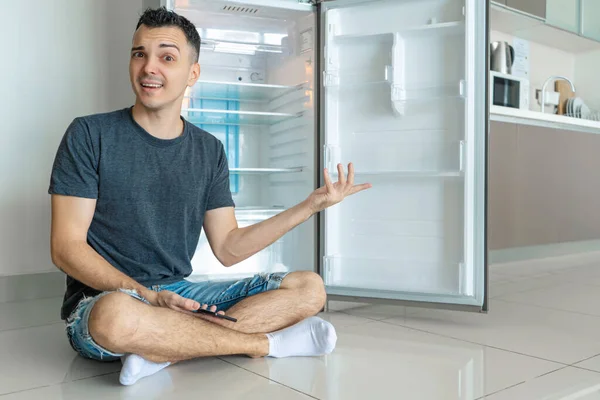 A young guy orders food using a smartphone. Empty refrigerator with no food. Food delivery service advertisement.