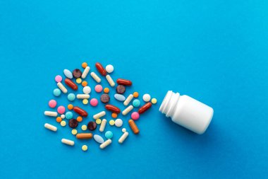 Bir avuç dolusu renkli hap mavi arka planda kutudan döküldü. Tıbbi konsept.