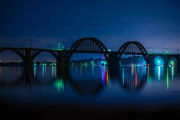 水の中に多くの色の光が反射して街の遊歩道の夜の風景 シルエットのザトウェイバック鉄道橋 — ストック写真