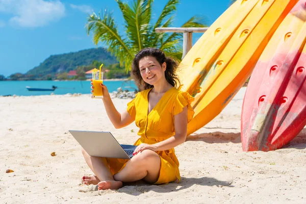 Дівчина Жовтій Сукні Тропічному Піщаному Пляжі Працює Ноутбуці Поблизу Каяків — стокове фото