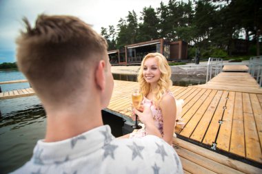 Romantik randevu sürprizi. Genç bir adam ve bir kız ahşap iskelede. Şampanyalı kadehleri kaldırın.