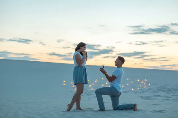 男は砂漠の砂の上に立っている間に膝を曲げ 少女に結婚の提案をします ろうそくは砂の中で燃える — ストック写真