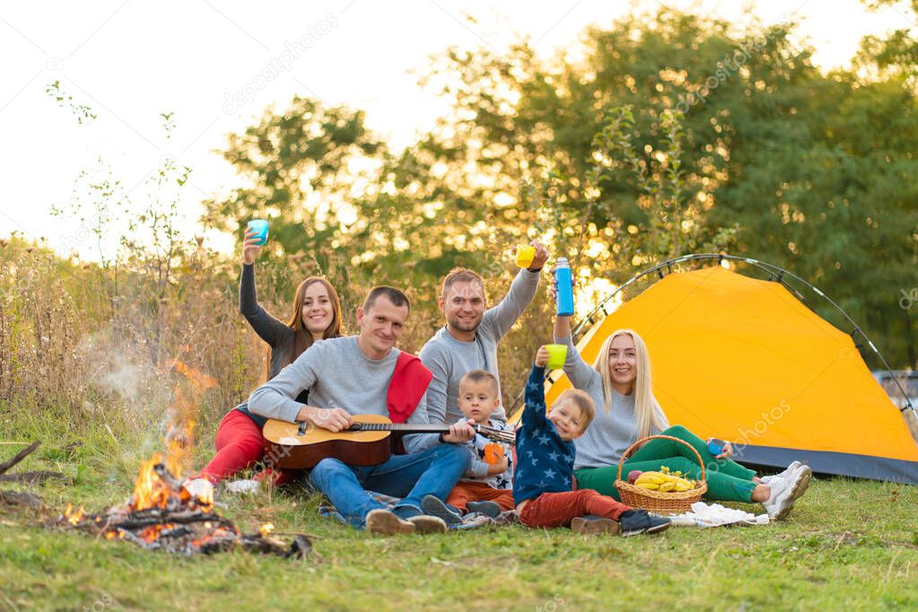 travel, tourism, hike, picnic and people concept - group of happy friends with tent and drinks playing guitar at camping.