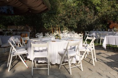 Pirinç bir vazoda taze çiçeklerle süslenmiş düğün masası. Düğün çiçekçisi olarak. Dışarıdaki yeşil manzaralı misafirler için bir ziyafet masası. Güllü buket, Eustoma ve okaliptüs yapraklı..