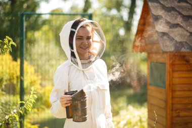 Beyaz takım elbiseli arı yetiştiricisi kız, bir arı içicisiyle bir ipucunun yanında poz veriyor..