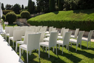 Güzel bir düğün hazırlığı. Romantik bir düğün töreni. Çimenli su manzaralı bir düğün. Düğün dekoru. Yeşil çimenlikteki beyaz tahta sandalyeler. Misafirler için beyaz koltuklar.