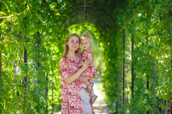 一个穿着淡淡的夏装的迷人女孩和她的小女儿在一个绿色的公园里散步 抱着她 享受温暖阳光明媚的夏日 — 图库照片