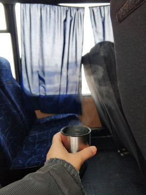Bir adam elinde, otobüsün kabininde sıcak çay buharı ile termostan bir şapka tutuyor. Yolculuk sırasında sıcak içecek..