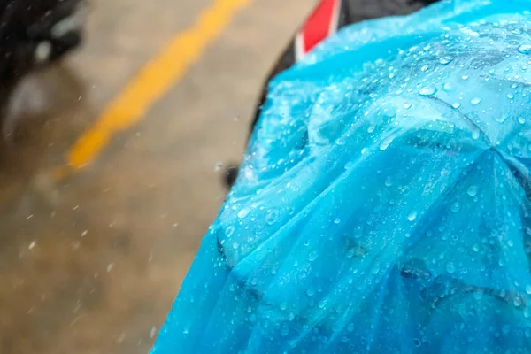 A close-up of a raindrop on a blue raincoat thrown onto a scooter during the rain.