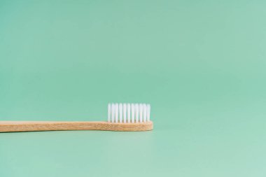 Çevre dostu bambu ahşap antibakteriyel diş fırçası açık yeşil arka planda.