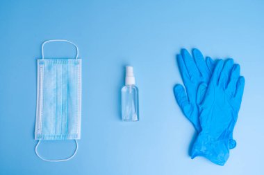 Tıbbi maske, eldiven ve mavi arka planda dezenfektan kişisel hijyen malzemeleri. COVID-19 salgını. İlaçlar..