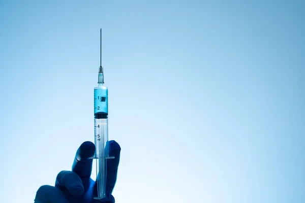 Tıbbi eldivenli bir el, içinde koronavirüs aşısı ve aşının içinde çip olan bir şırınga taşır. Komplo teorisi. İnsanları yontmak.