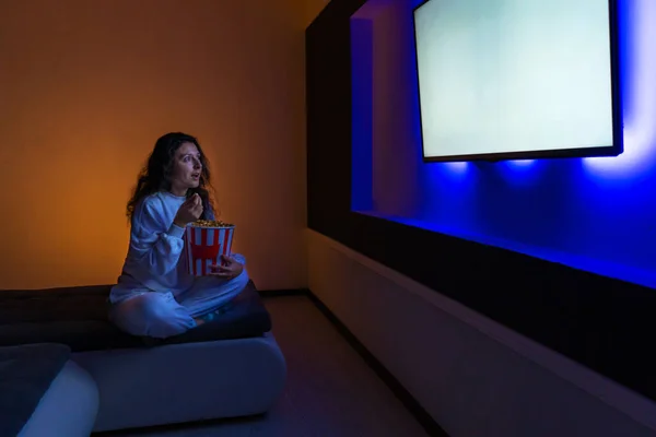 person watches a movie sitting on the couch with a bucket of popcorn.