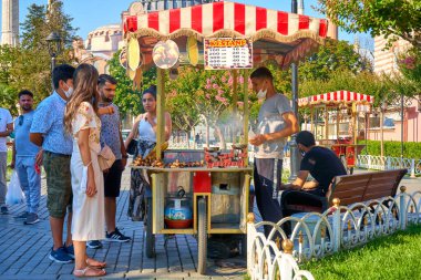 İstanbul 'da yaz caddesinde el arabasından ızgara mısır satan bir adam. Türk sokak yemekleri işi. Türkiye, İstanbul - 21.07.2020