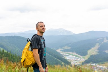 Sarı sırt çantasıyla gezen bir adam güzel dağ manzaralı güzel yerlerde gezer..