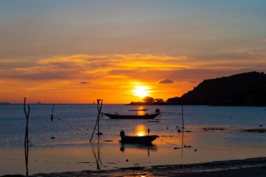 Tayland 'da tropik bir adanın sahilinde güzel bir gün batımı, okyanustaki bir teknenin silueti..