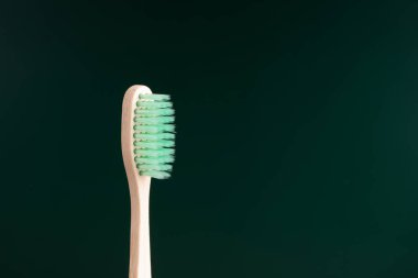 Çevre dostu antibakteriyel bambu ahşap diş fırçası koyu yeşil arka planda. Eğilimde çevrenin korunması.