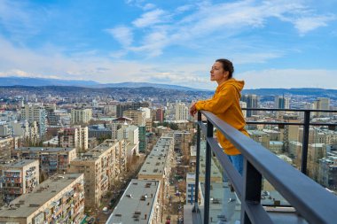 Güzel kız gökdelenin yüksek katının balkonunda dikilirken poz veriyor..