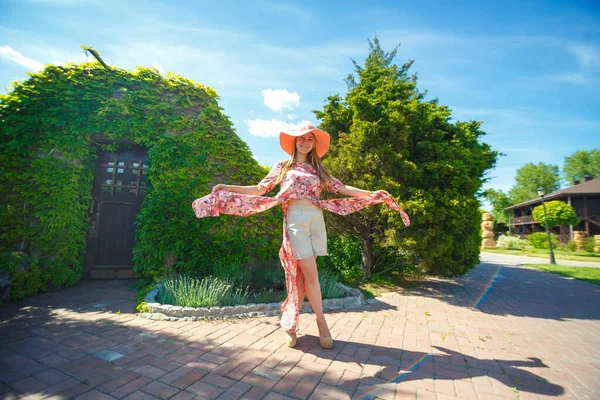 明るい夏の日差しの中でチャーミングな女の子とパレオの帽子は緑の公園を歩いています 暖かい晴れた夏の日を楽しむ — ストック写真