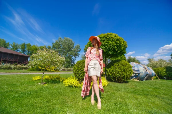 明るい夏の日差しの中でチャーミングな女の子とパレオの帽子は緑の公園を歩いています 暖かい晴れた夏の日を楽しむ — ストック写真