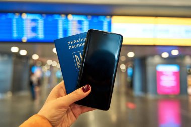 Pasaport ve telefon, havaalanı bilgi panosunun arka planında. En az malla seyahat et.