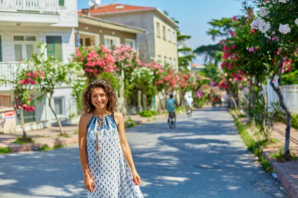 魅力的なブルネットの女の子がトルコのブユカダ島の通りを歩いています 夏の晴れた日と開花の木 — ストック写真