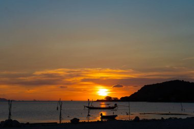 Tayland 'da tropik bir adanın sahilinde güzel bir gün batımı, okyanustaki bir teknenin silueti..