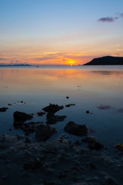 Deniz kıyısında gün batımının muhteşem manzarası, günbatımının renkleri ve sudaki adanın silueti. İnanılmaz tropikal gün batımı.
