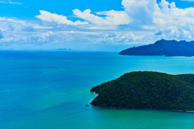 Uçak penceresinden okyanusta yeşil bir tropikal adanın görüntüsü.