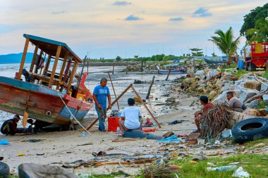 Balıkçı köyündeki kumlu nehir kıyısında eski bir tekne. Asya 'da bir adada balıkçı köyü. Langkawi, Malezya - 06.23.2020