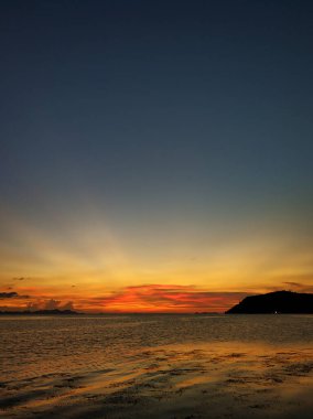 Okyanus kıyısında bulutlu, yakıcı gün batımı.