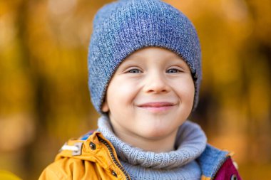 Mutlu çocuk, sonbaharda parkta yürürken düşmüş sarı yapraklarla oynuyor..