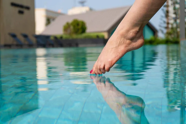 Close-up of a girl's leg descends into the pool. The foot touches the water. Checks the water temperature before swimming.