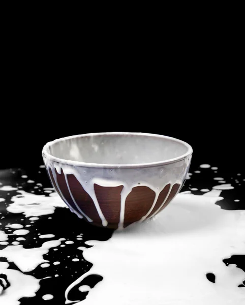 Ceramic bowl and spilled milk in black — Stok Foto