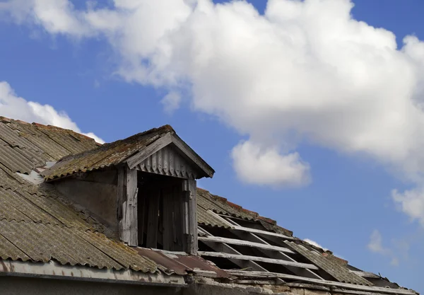 Old tile roof with holes and blue sky with clouds — Stock Photo, Image